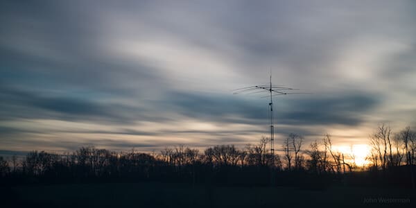 Background image of a SteppIR antenna and treeline silhouetted from a sunset